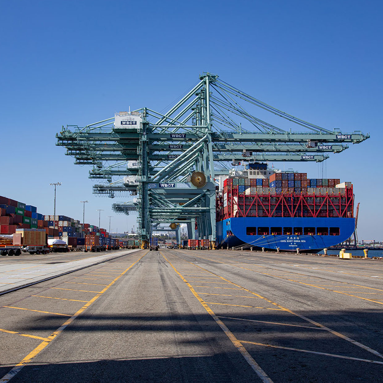 Several large cranes unload containers from a docked cargo ship at a busy port.